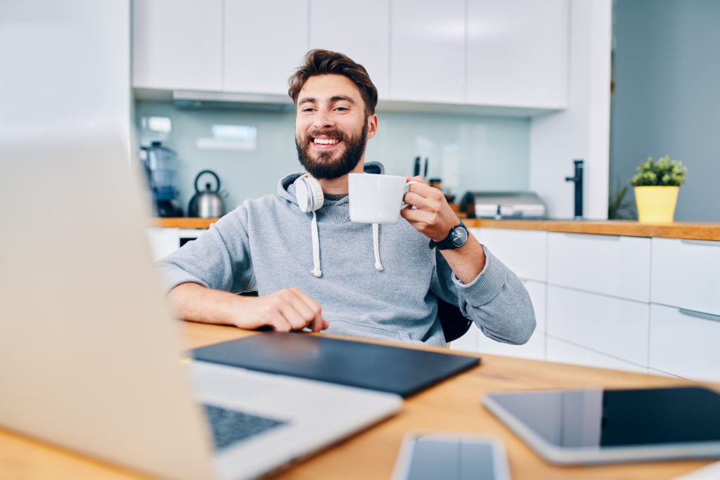 Joyful young web developer drinking coffee while taking break from working from home