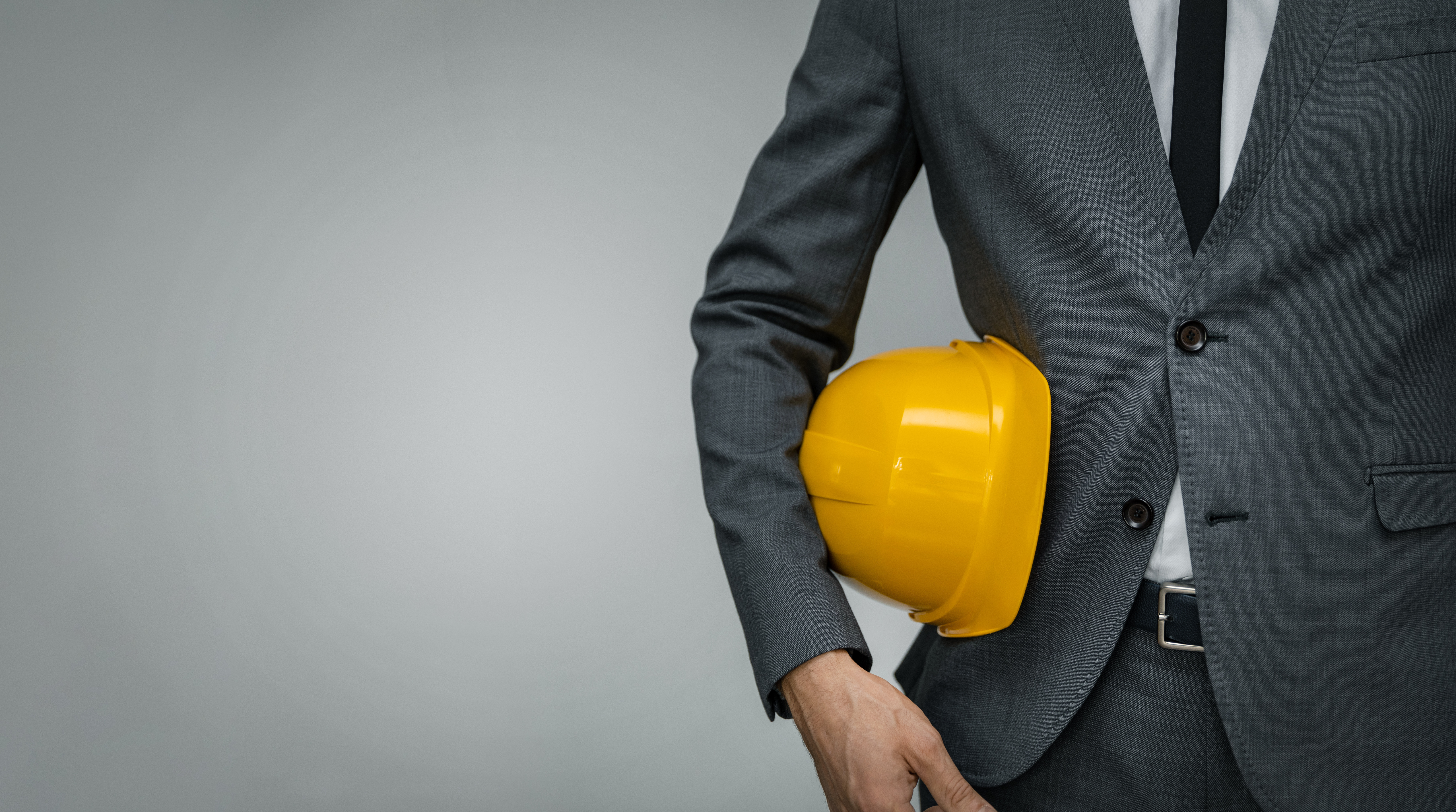 Management Liability construction industry business - businessman holding yellow hard hat underarm on gray background with copy space