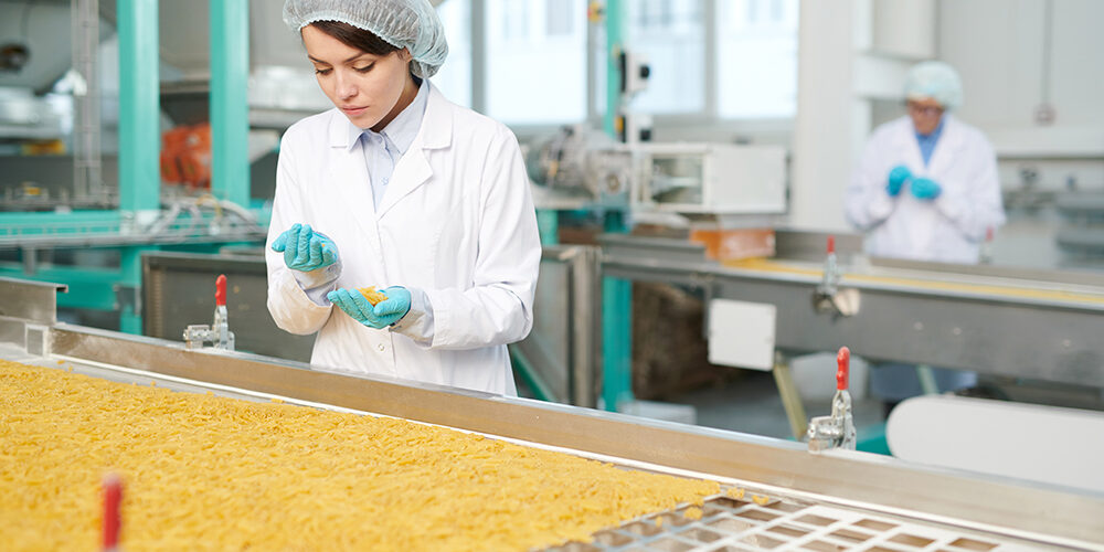 Portrait of pretty young woman working at modern food factory and inspecting macaroni on production line, copy space