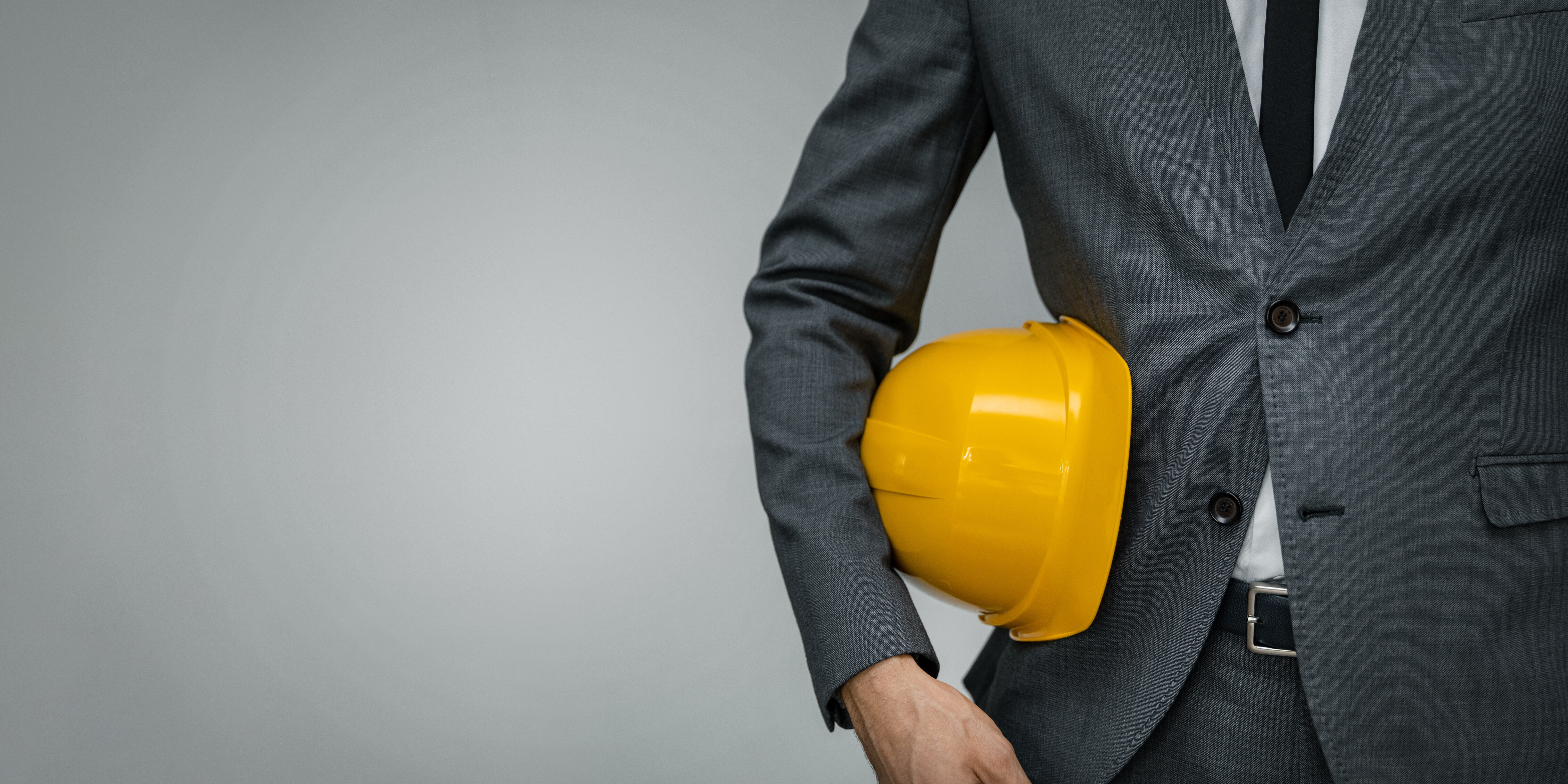 construction industry business - businessman holding yellow hard hat underarm on gray background with copy space